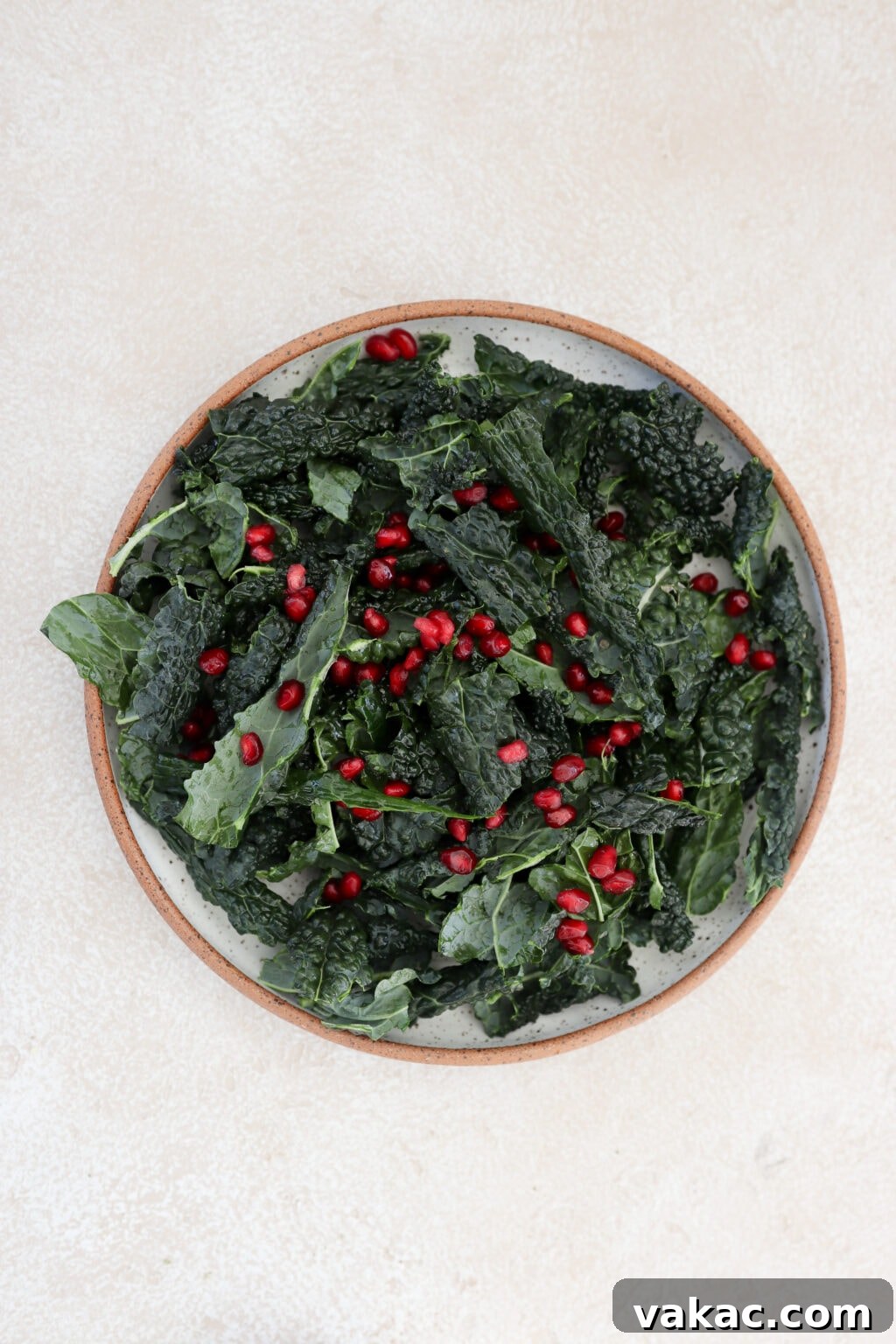 A speckled grey bowl containing massaged kale and bright red pomegranate arils distributed over the greens.