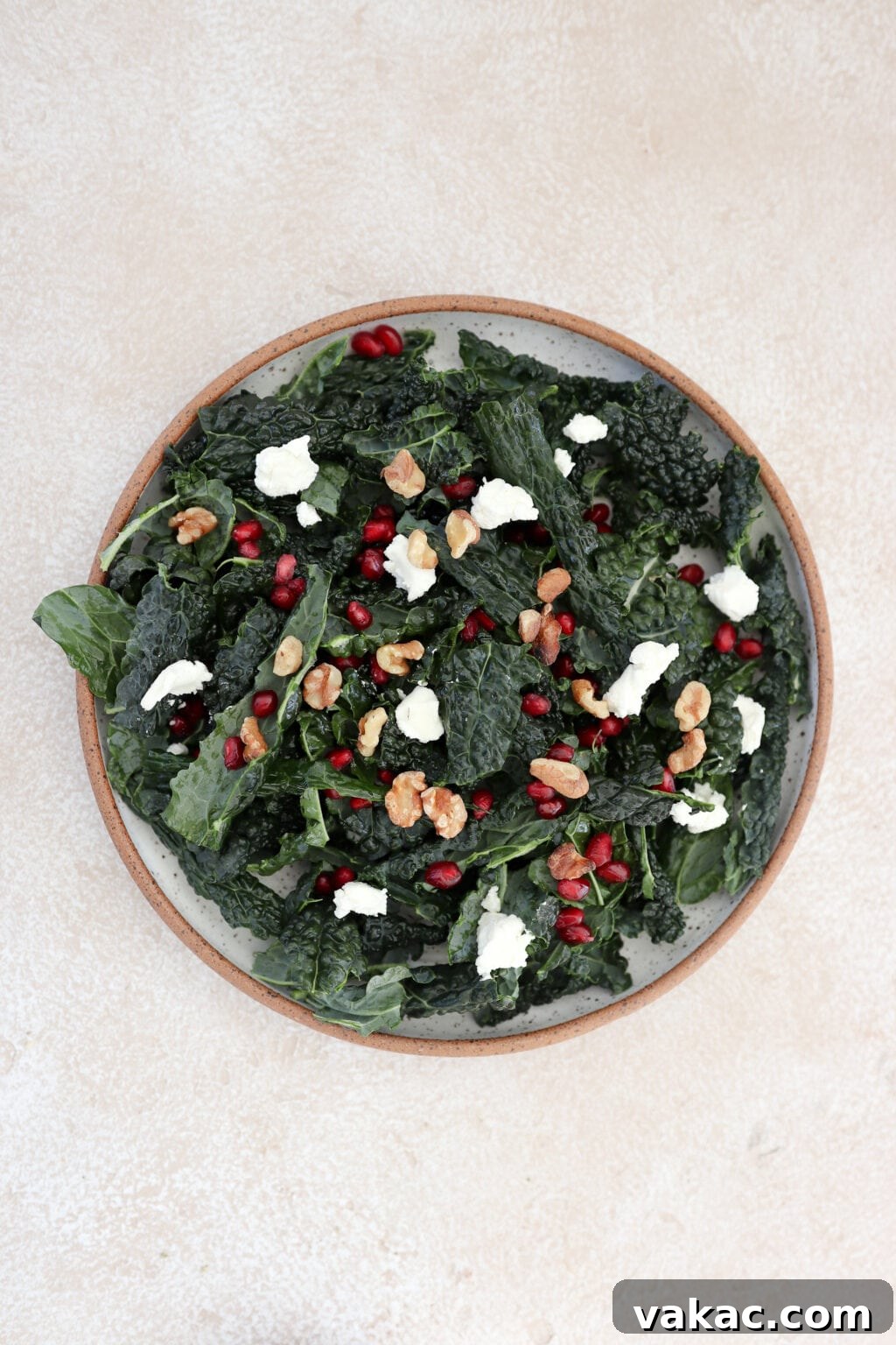 A close-up of a kale and pomegranate salad topped with crumbled goat cheese and toasted walnuts.