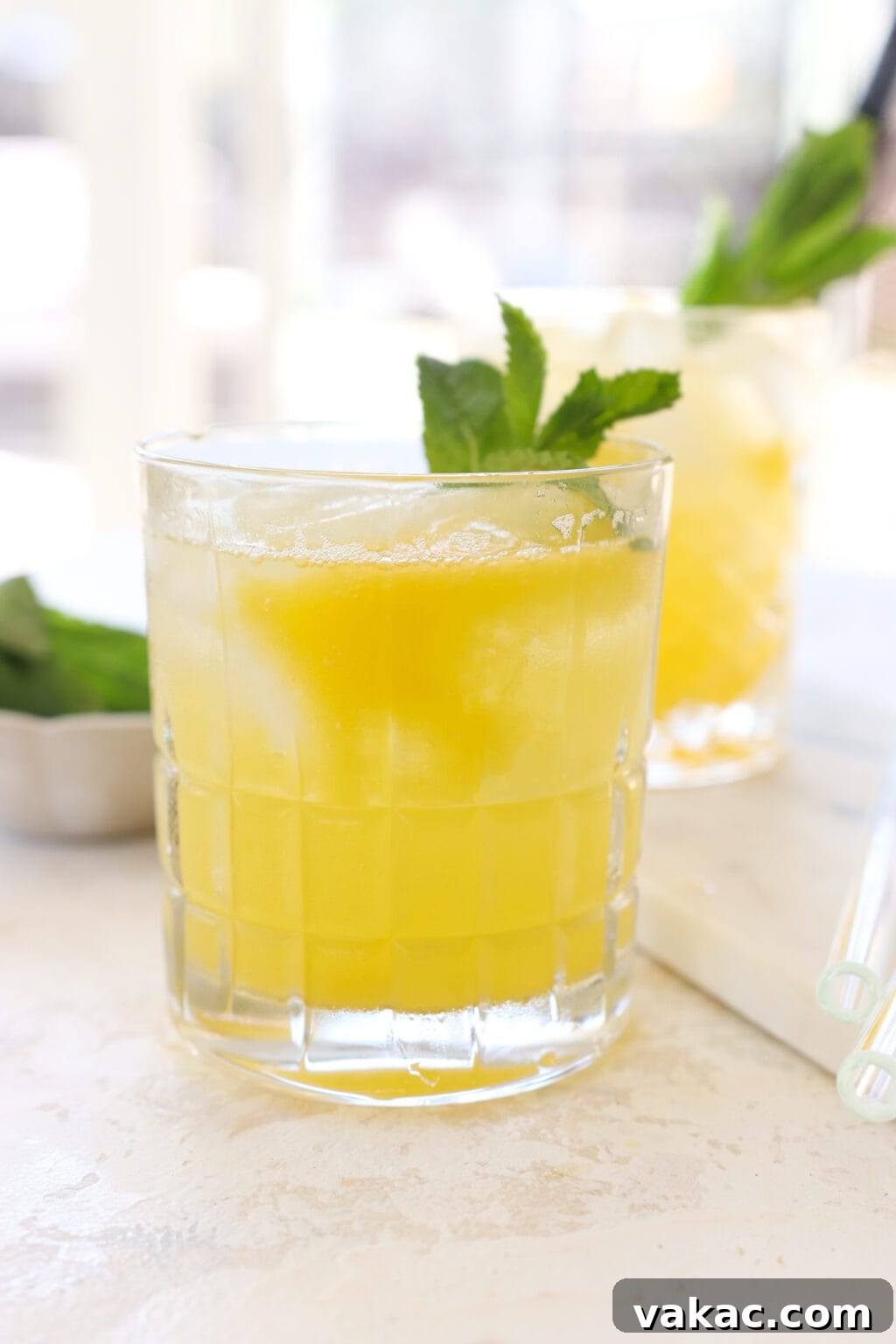 Effortless Wholesome Mango Puree 2 A refreshing glass of sparkling water topped with homemade mango puree and garnished with fresh mint, with another similar glass blurred in the background.