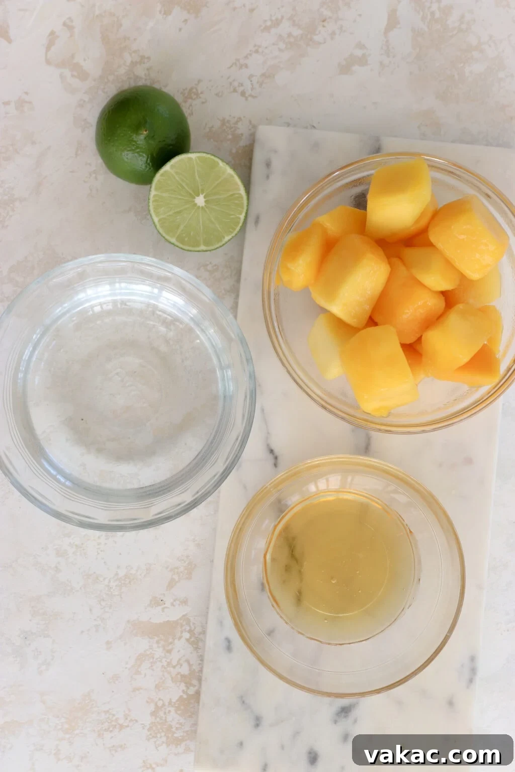 Effortless Wholesome Mango Puree 3 An overhead view of the simple ingredients needed for mango puree: two lime halves, a bowl of cubed mango, a bowl of water, and a bowl of honey.