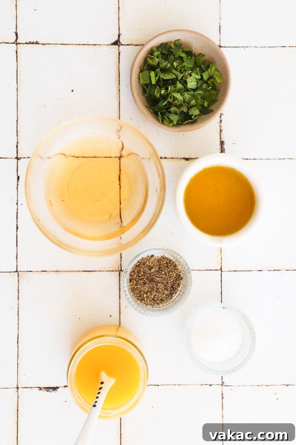 Zesty 5-Minute Mango Mint Vinaigrette 3 An overhead shot showcasing the fresh ingredients required for mango and mint salad dressing: a bowl of chopped mint, olive oil in a clear container, white wine vinegar in a white bowl, small glass bowls of salt and pepper, and a jar of homemade mango puree.