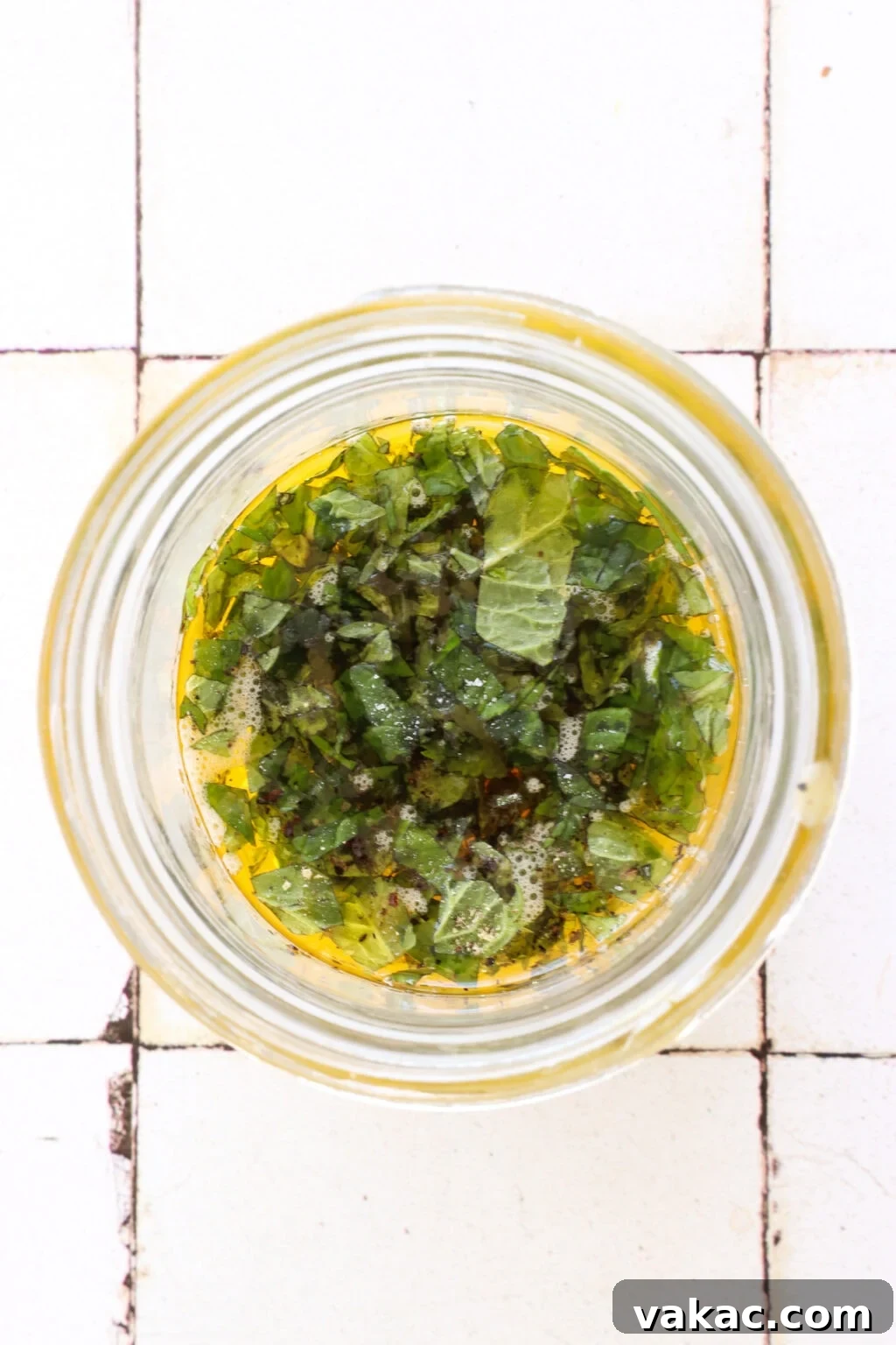Zesty 5-Minute Mango Mint Vinaigrette 4 A glass bowl on a white tile counter holds the measured ingredients: olive oil, white wine vinegar, mango puree, and finely minced mint leaves, ready to be combined.