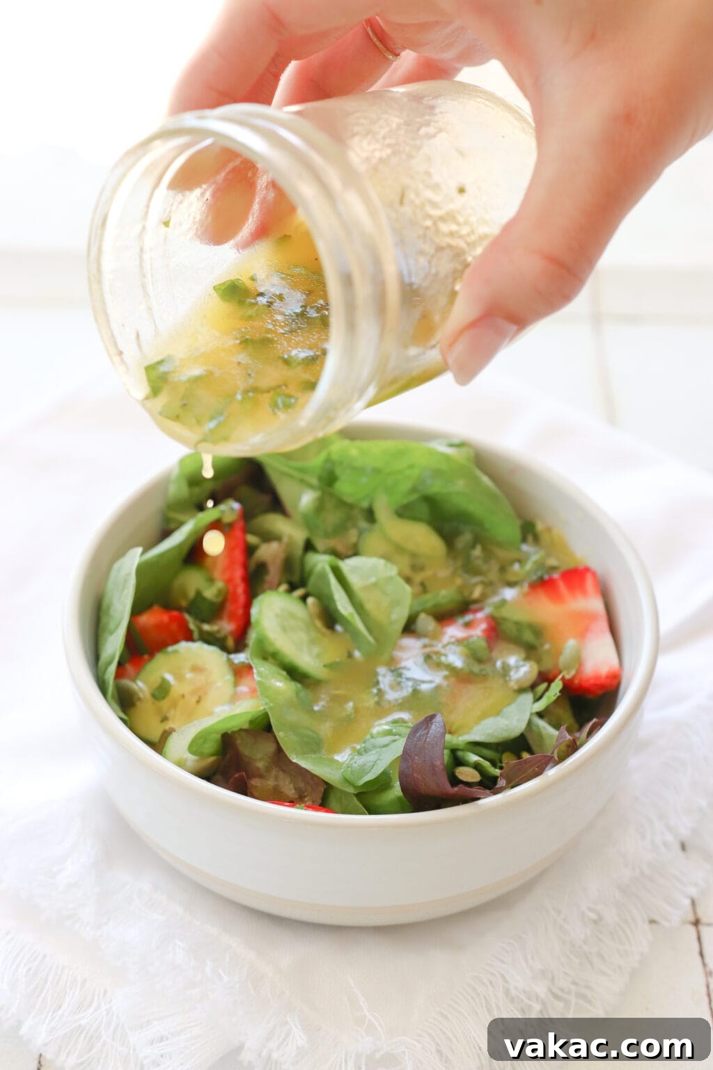 Zesty 5-Minute Mango Mint Vinaigrette 6 A hand holds a glass mason jar, gracefully pouring the vibrant mango salad dressing over a fresh mixed green and strawberry salad, creating an inviting visual of culinary delight.