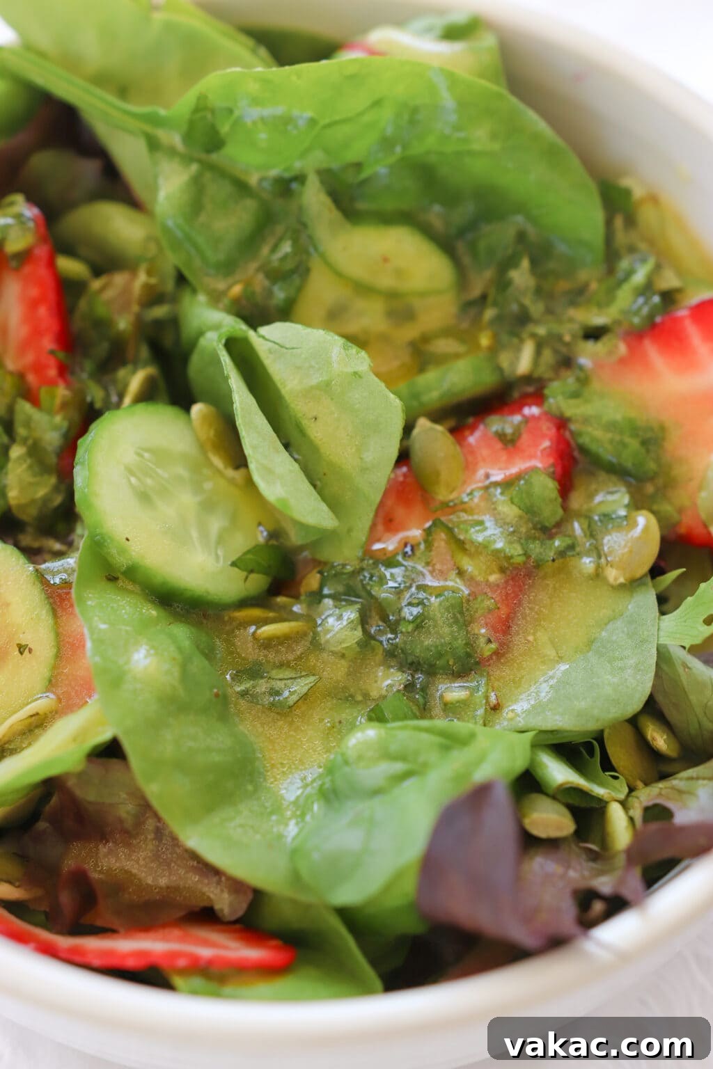 Zesty 5-Minute Mango Mint Vinaigrette 7 A zoomed-in photo captures a tantalizing mixed green salad, adorned with vibrant strawberries and perfectly dressed in the luscious yellow mango mint vinaigrette, highlighting its appetizing appeal.