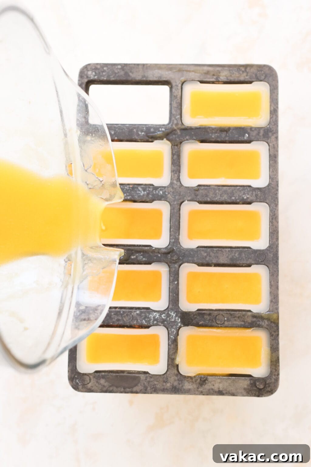 Sweet Heat Mango Tajin Popsicles 5 An overhead view shows an orange-yellow liquid being carefully poured from a blender into multiple popsicle molds, filling each one evenly.