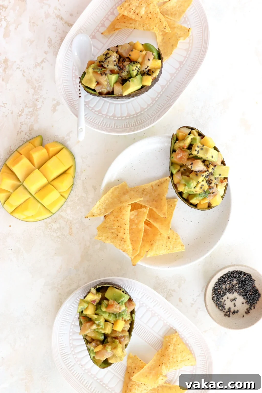 An overhead shot of 3 tuna avocado boats on white plates. There is a scored mango and a bowl with black sesame seeds.