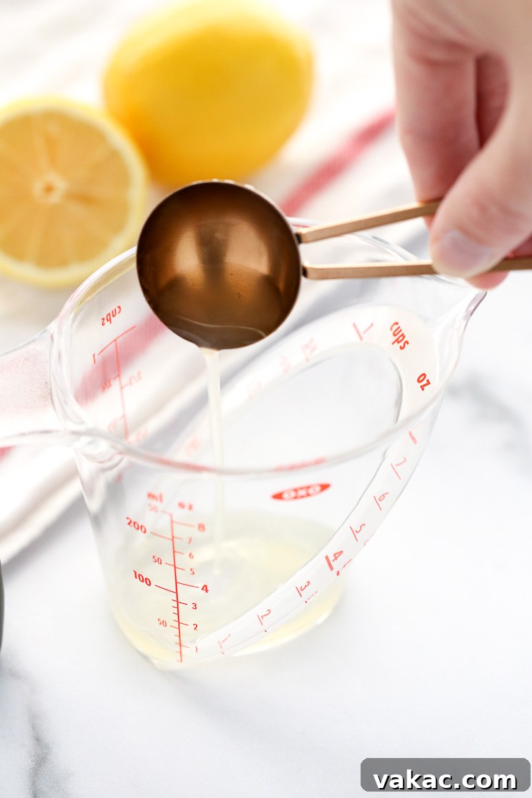 Whip Up Your Own Buttermilk 4 A clear measuring cup containing one tablespoon of fresh lemon juice, with a white napkin and lemons in the background.