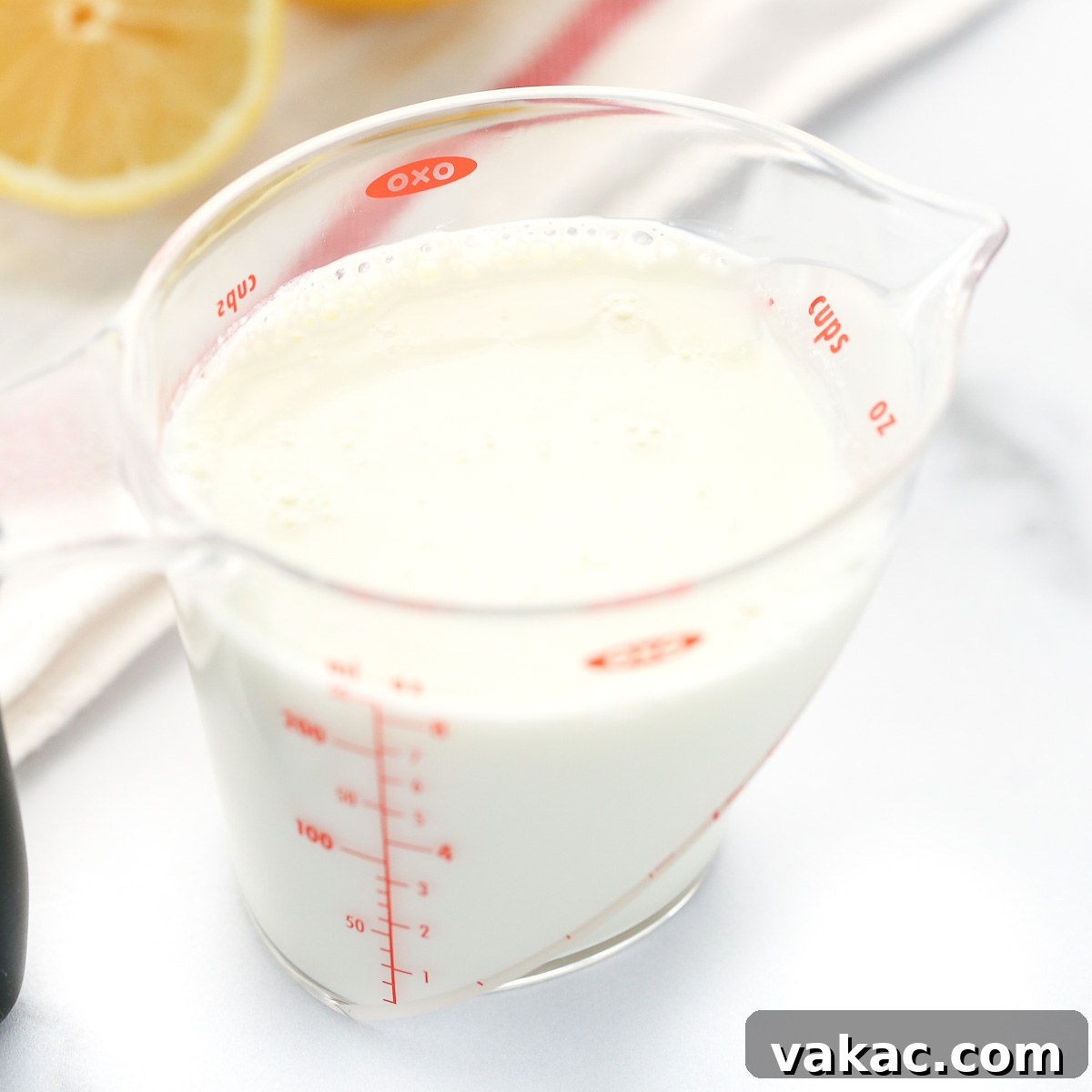 A clear measuring cup filled with homemade buttermilk, along with a white napkin and lemons in the background.