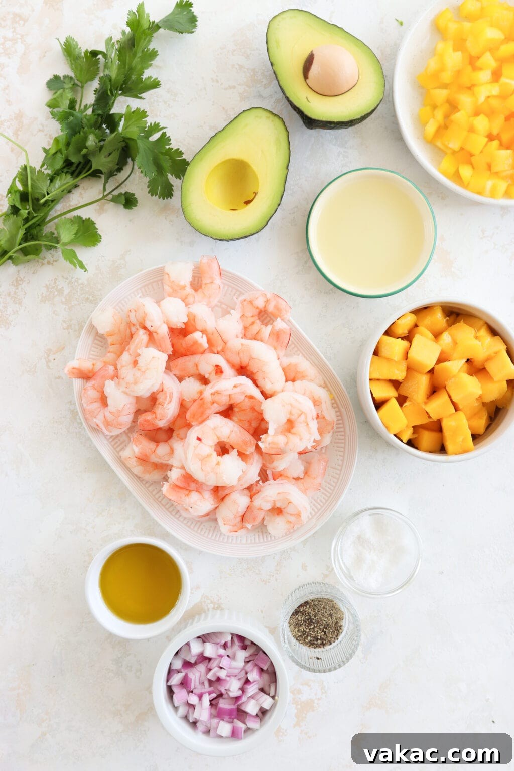 Speedy Prawn Ceviche with Vibrant Mango Avocado 3 An overhead flat lay of the fresh ingredients needed for a Prawn, Mango, and Avocado Salad. From top left to right: a vibrant bunch of cilantro, a perfectly ripe avocado half, a lime, and neatly cubed yellow bell pepper. Below these, bright pink shrimp are alongside precisely cubed mango. The bottom row displays essential dressing components: olive oil, finely diced red onion, black pepper, and a pinch of salt.