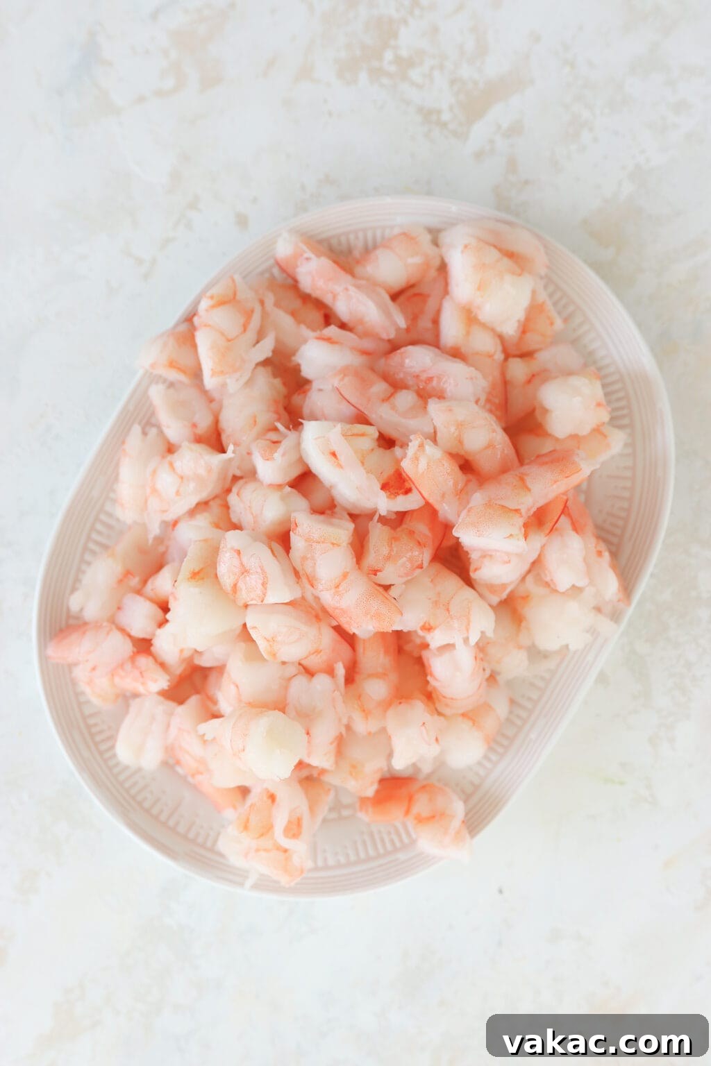 Speedy Prawn Ceviche with Vibrant Mango Avocado 4 A white plate set against a marble background, showcasing a pile of vibrant pink shrimp. The shrimp has been expertly chopped into thirds, ready for salad preparation.