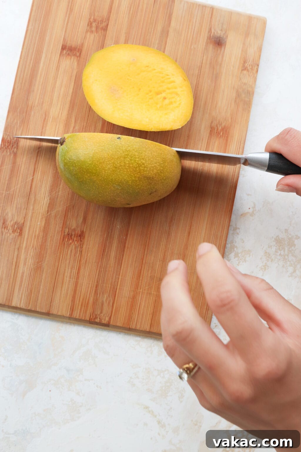 Easy Quick Pickled Mango Recipe 5 A single mango half, cleanly cut with the flat side facing up, rests on a wooden cutting board with a chef's knife beside it, ready for the next cut.