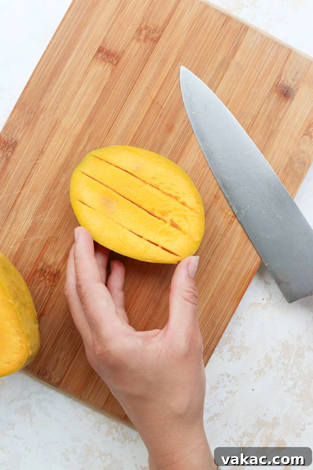 Easy Quick Pickled Mango Recipe 6 A mango half on a wooden cutting board has been scored lengthwise with precise cuts, with a hand steadying it, ready for the next step.