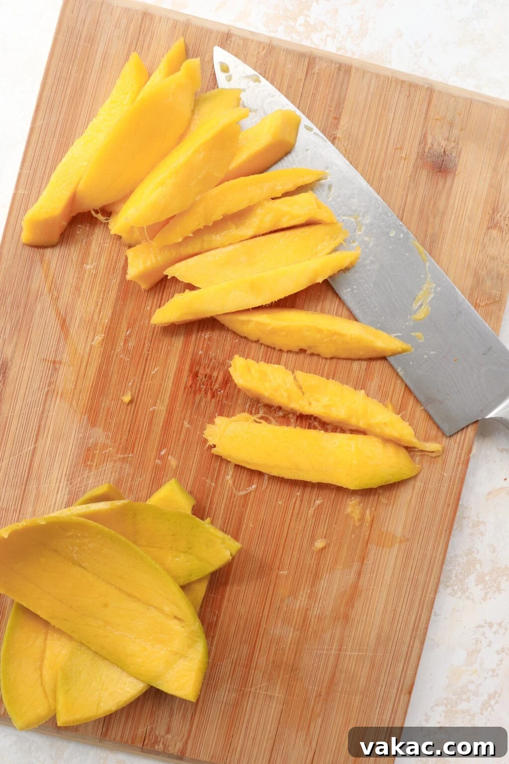 Easy Quick Pickled Mango Recipe 7 Bright orange mango slices, perfectly sized for pickling, are fanned out on a wooden cutting board next to a chef's knife and the discarded mango skin.