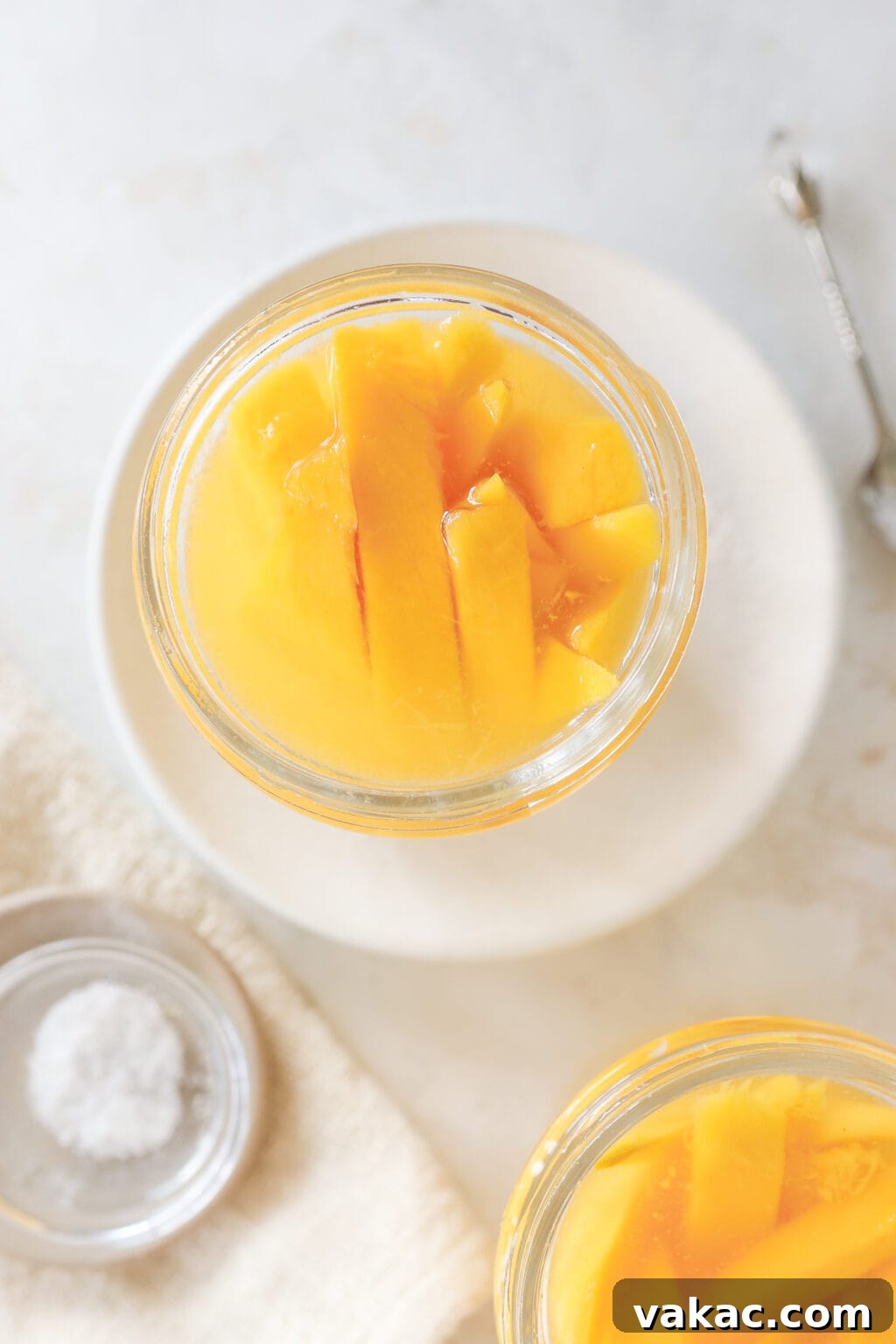 Easy Quick Pickled Mango Recipe 9 An overhead shot shows a mason jar filled with mango slices and pickling liquid, with a small bowl of salt nearby, indicating the brine preparation.