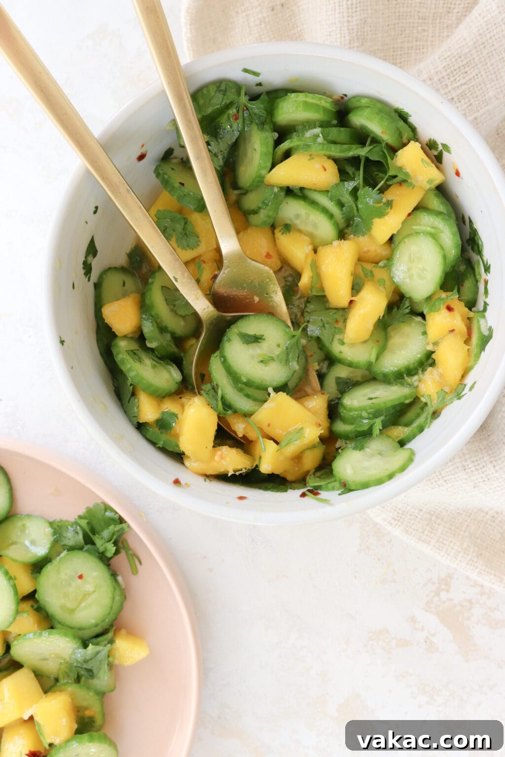 Bright Bites: 5-Minute Mango and Cucumber Salad 6 A vibrant cucumber and mango salad served in a white bowl, with two elegant gold spoons ready for serving.