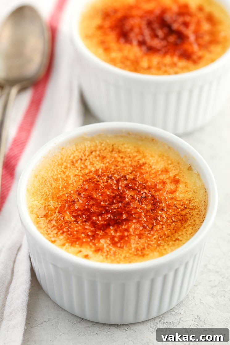 Crème Brûlée Made Simple 2 Two white ramekins filled with homemade crème brûlée and a white napkin and two spoons on the side, highlighting the crisp caramelized topping.