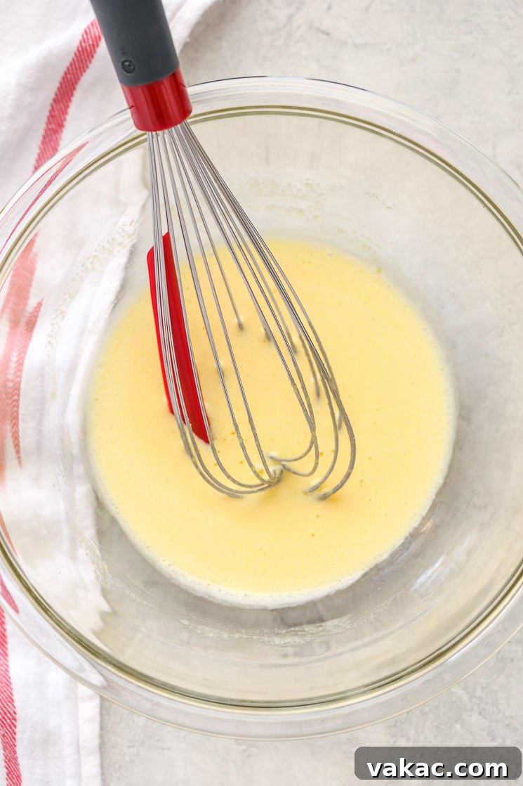 Crème Brûlée Made Simple 3 A clear glass bowl filled with egg yolks whisked with sugar and a white napkin on the side, showing the pale yellow color of the mixture.