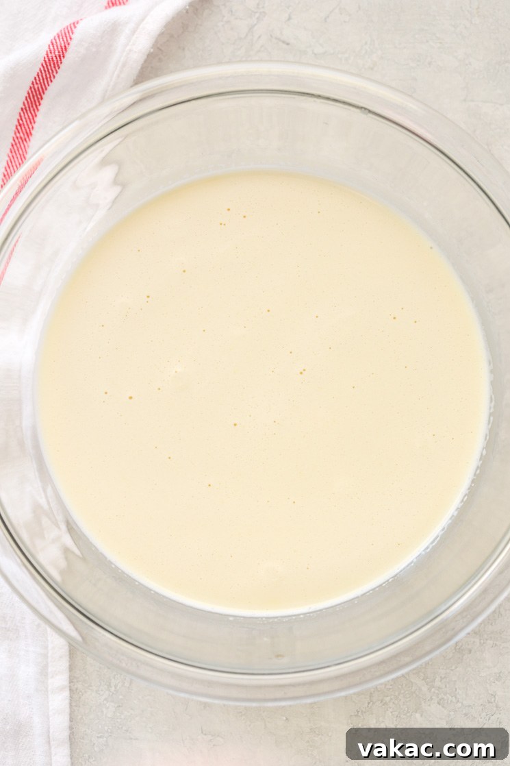 Crème Brûlée Made Simple 4 A clear glass bowl filled with the crème brûlée mixture, a smooth light yellow liquid, with a white napkin on the side of the bowl.
