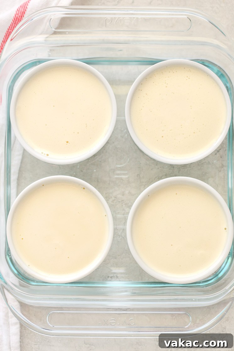 Crème Brûlée Made Simple 5 An 8-inch square glass baking dish with four white ramekins filled with the crème brûlée mixture, sitting in a water bath, ready for baking.