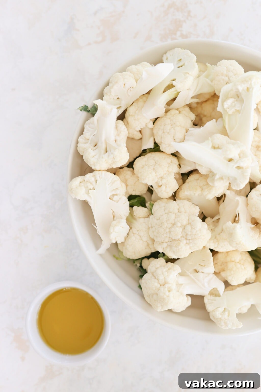 Meal Prep Magic Healthy Roasted Cauliflower Made Easy 3 A white bowl holds cauliflower florets. Beside it is a white ramekin with brown oil in it.