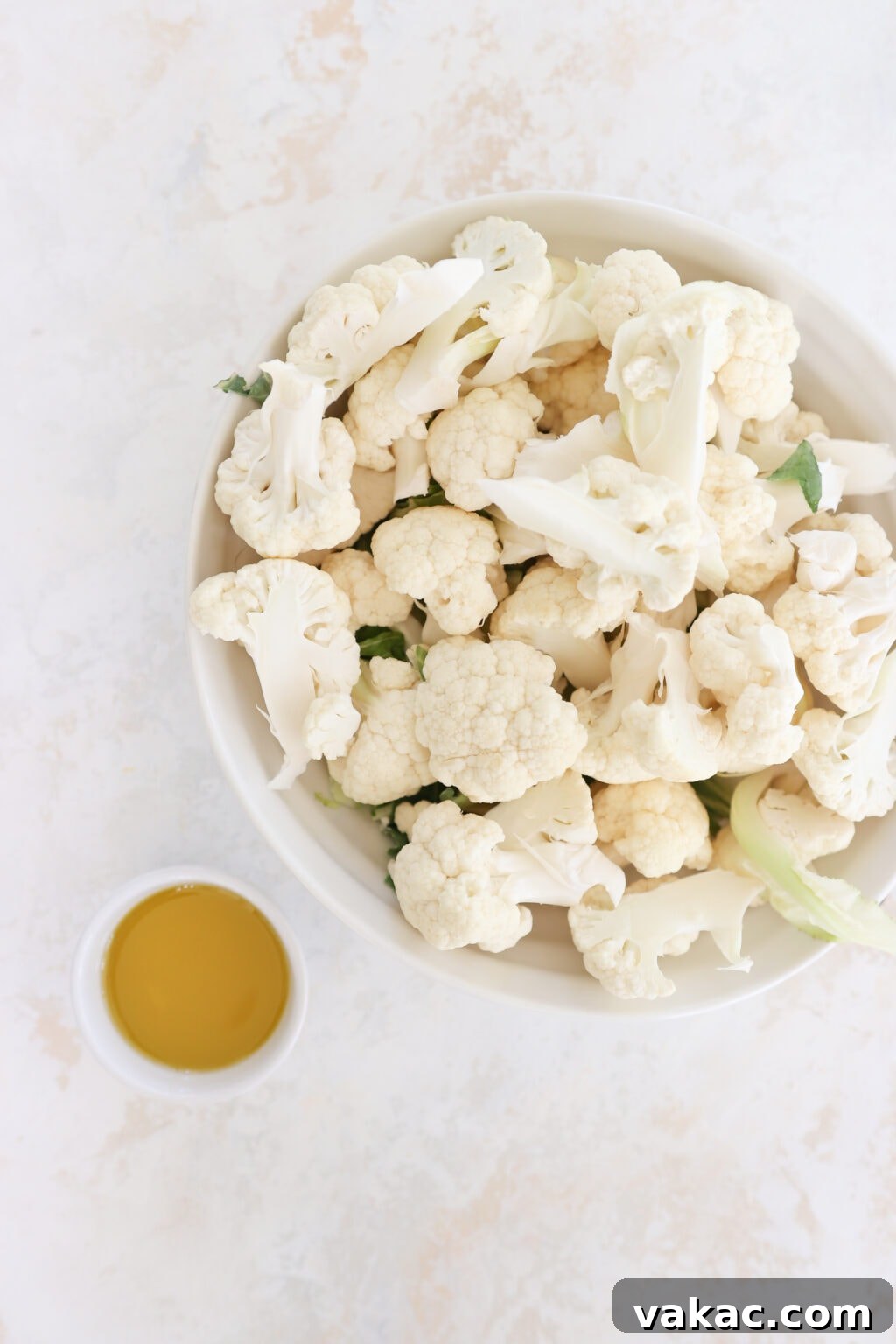 Meal Prep Magic Healthy Roasted Cauliflower Made Easy 4 A white bowl holds cauliflower florets. Beside it is a white ramekin with brown oil in it.