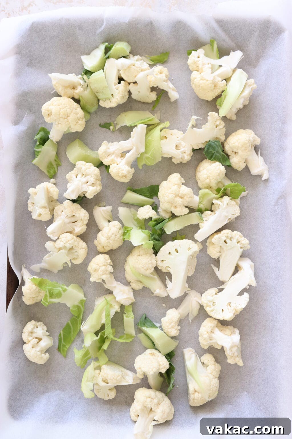 Meal Prep Magic Healthy Roasted Cauliflower Made Easy 5 Raw cauliflower florets are on a parchment lined baking sheet. The cauliflower greens are also on the baking sheet.