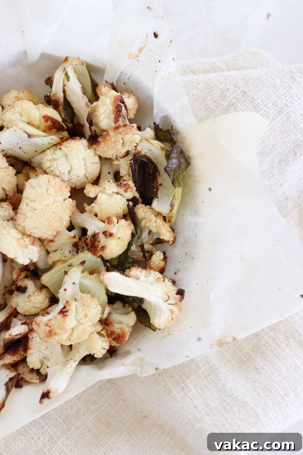Meal Prep Magic Healthy Roasted Cauliflower Made Easy 9 A zoomed in photo of roasted cauliflower in a parchment-lined bowl. It sits on a greyish white towel.