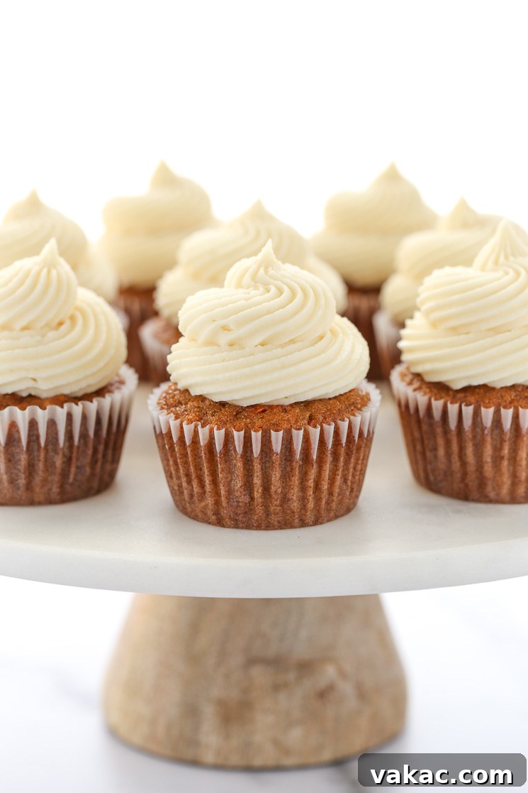 Spiced Carrot Cupcakes 2 A group of carrot cake cupcakes topped with cream cheese frosting resting on top of a marble cake stand with wooden base.