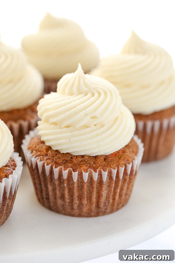Spiced Carrot Cupcakes 6 A close up picture of carrot cake cupcakes topped with cream cheese frosting sitting on top of a marble cake stand.