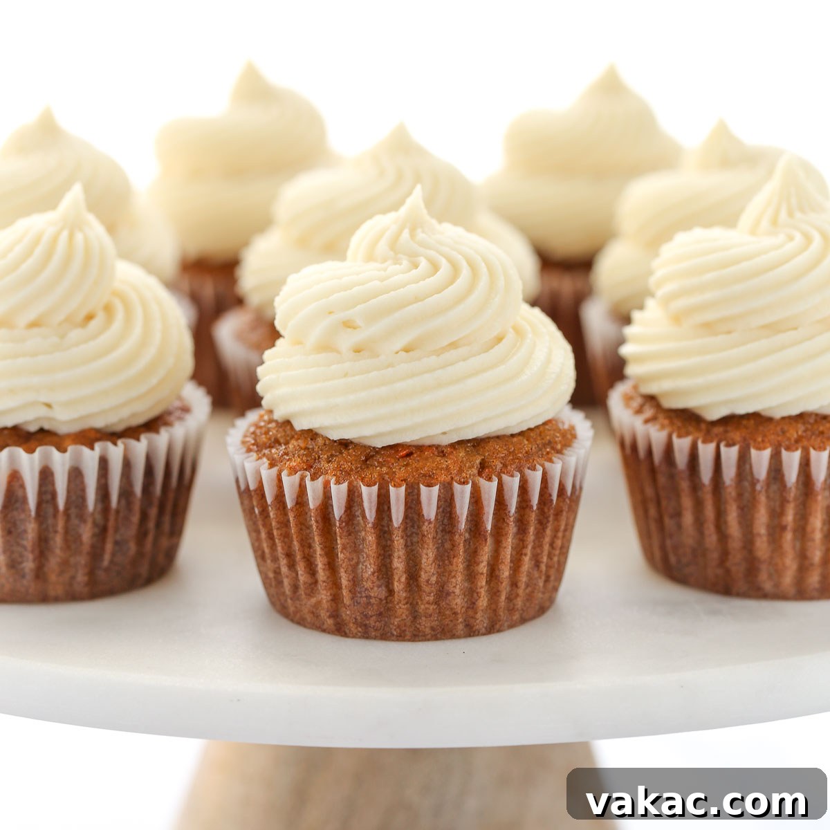 Spiced Carrot Cupcakes 7 A group of carrot cake cupcakes topped with cream cheese frosting setting on top of a marble cake stand.