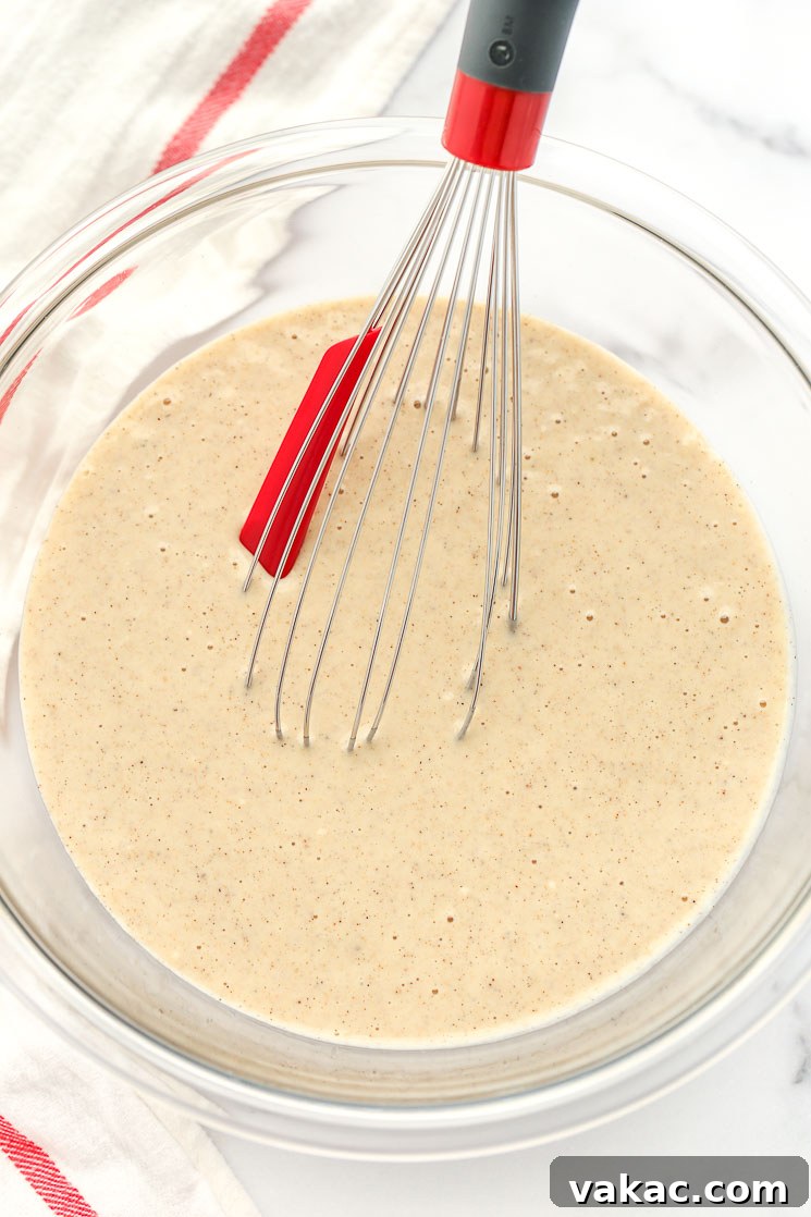 A clear glass bowl filled with funnel cake batter and a whisk.