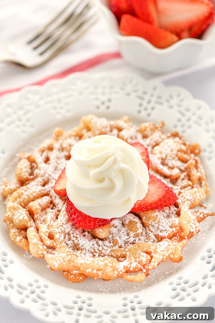 A homemade funnel cake topped with strawberries and homemade whipped cream sitting on a decorative white plate.