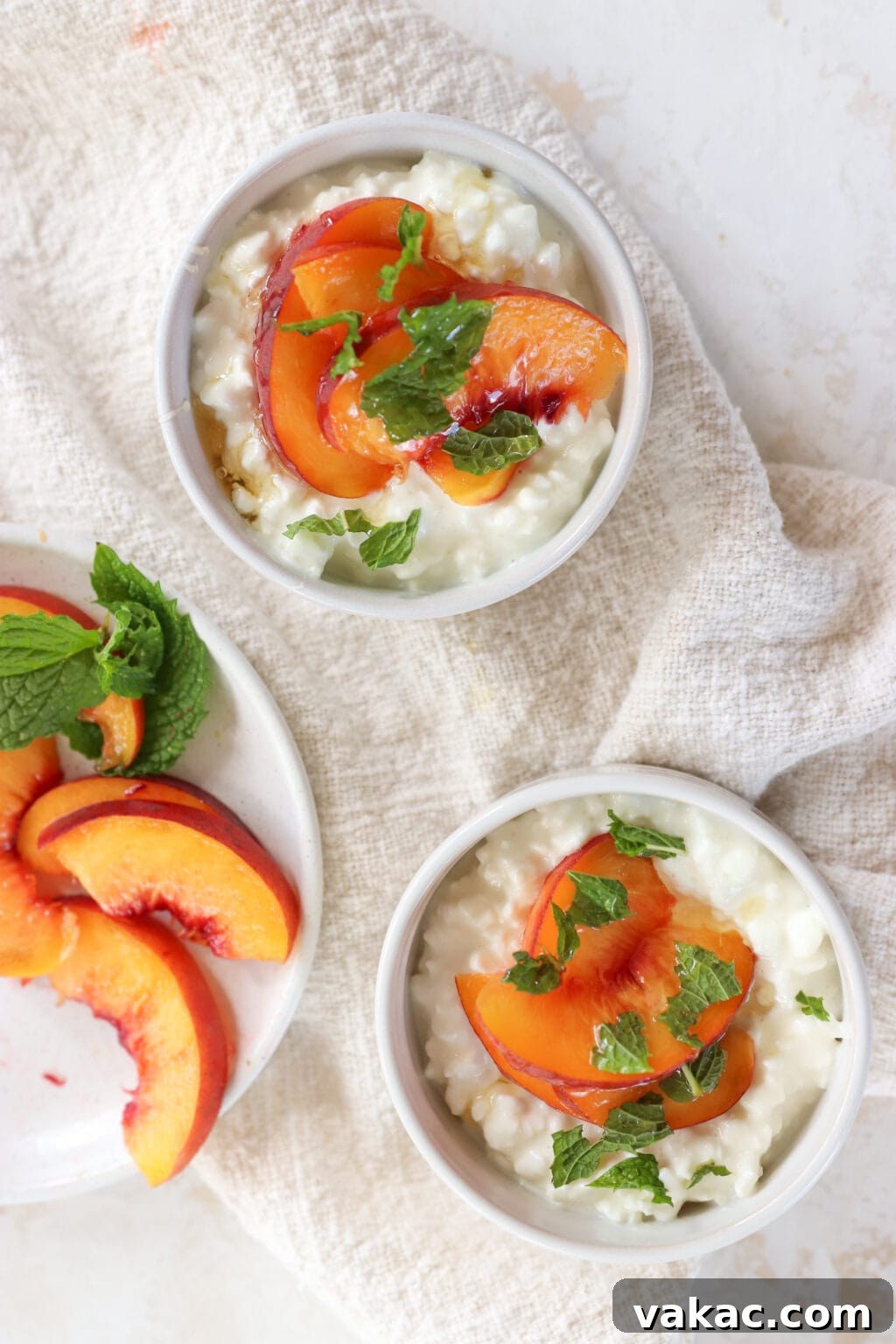 Two white bowls are filled with cottage cheese, sliced peaches and mint. To the left of the bowls is a plate of sliced peaches with mint.