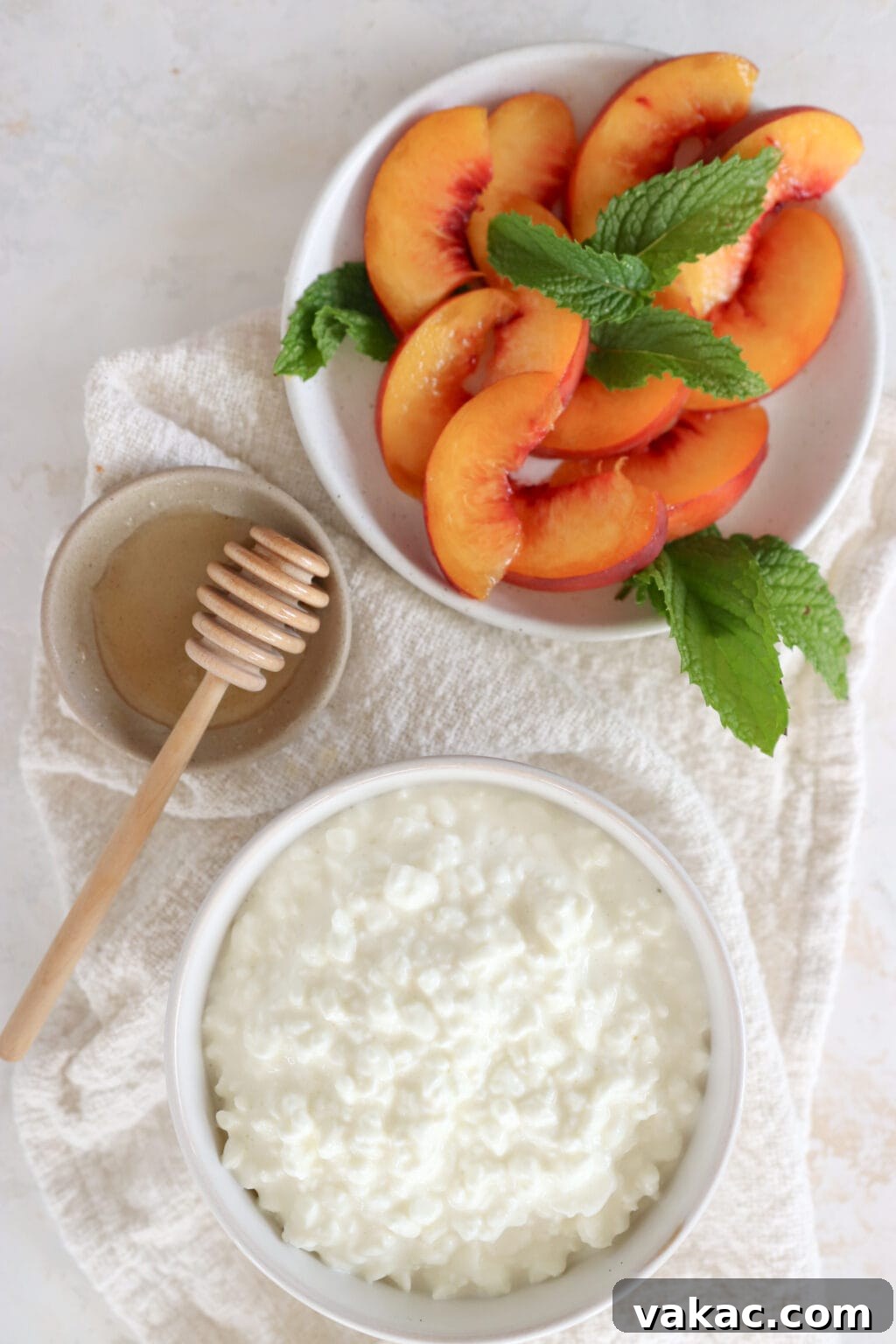 An overlay image of ingredients to make a cottage cheese snack with peaches, mint and honey. In the top-right hand corner is a plate of sliced peaches and mint leaves. Below on a light grey dish is honey with a honey twirler and in the bottom is a white bowl with cottage cheese in it.