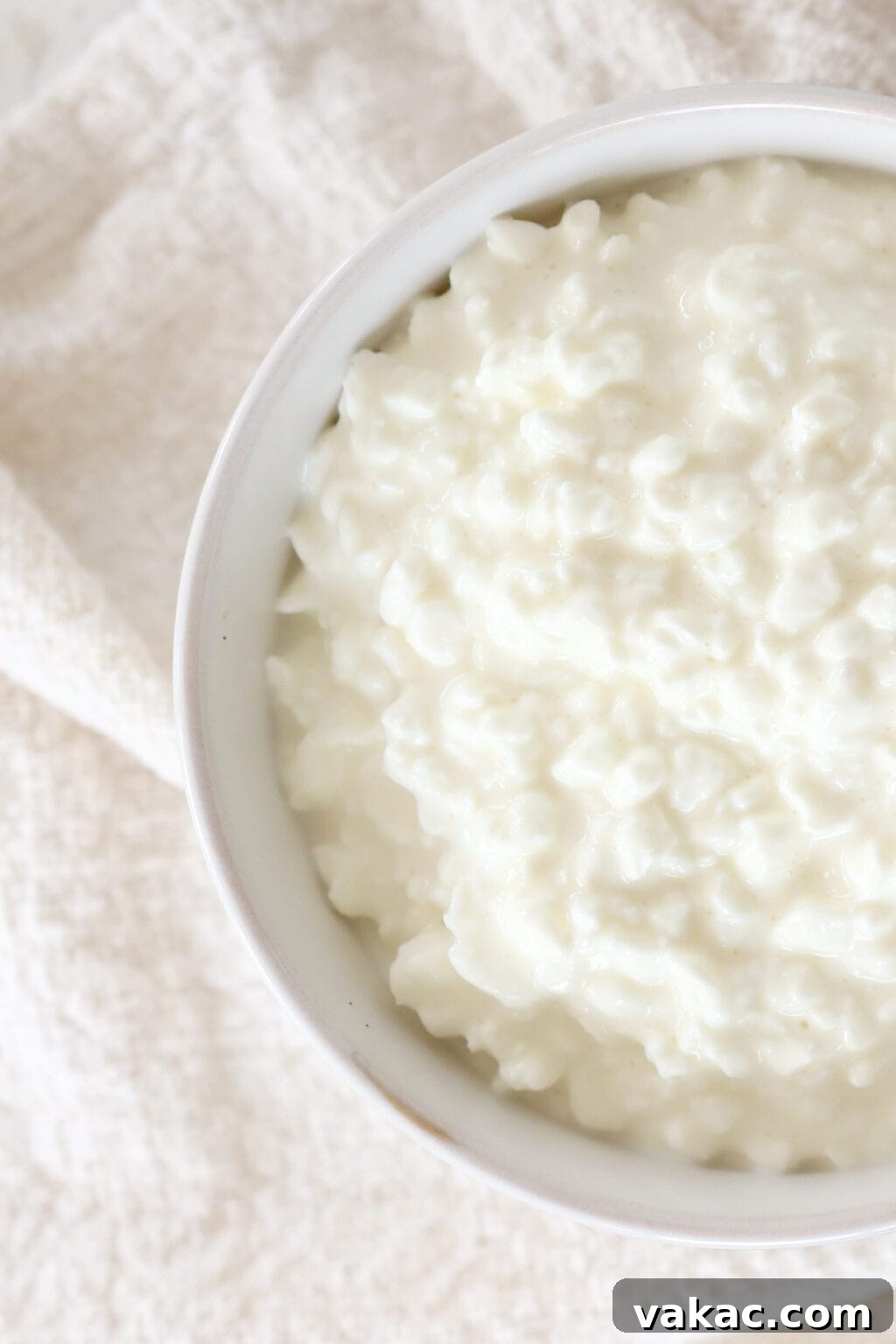 A zoomed in image of a white bowl with cottage cheese inside. The bowl is sitting on a textured dish towel.