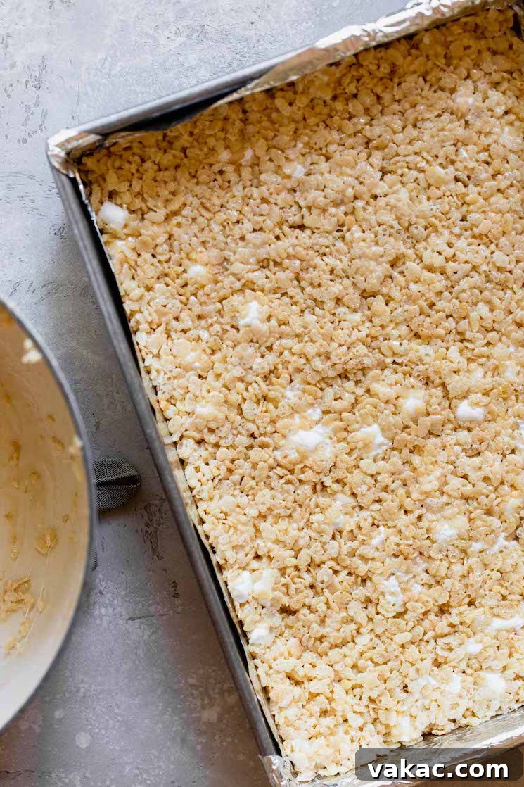 A metal baking pan filled with the warm, pressed Rice Krispie Treat mixture, cooling and setting into a delicious dessert.