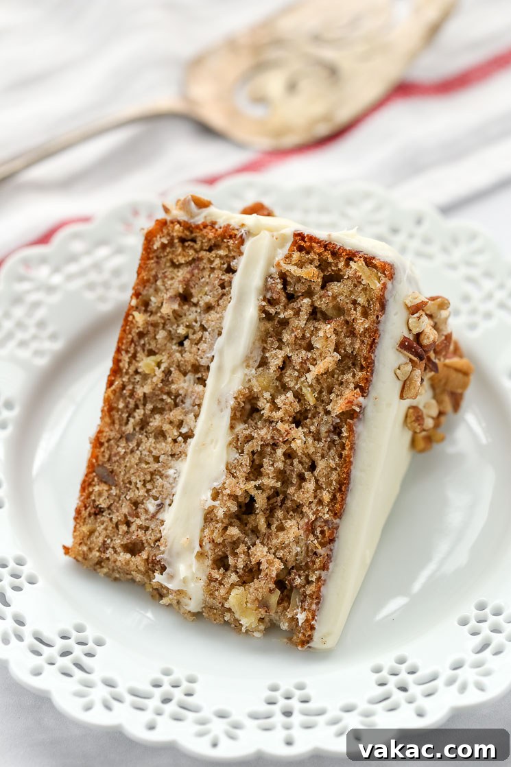 A single, perfectly cut slice of homemade hummingbird cake on an elegant white plate, with a cake server positioned gracefully in the background, showcasing its inviting layers.