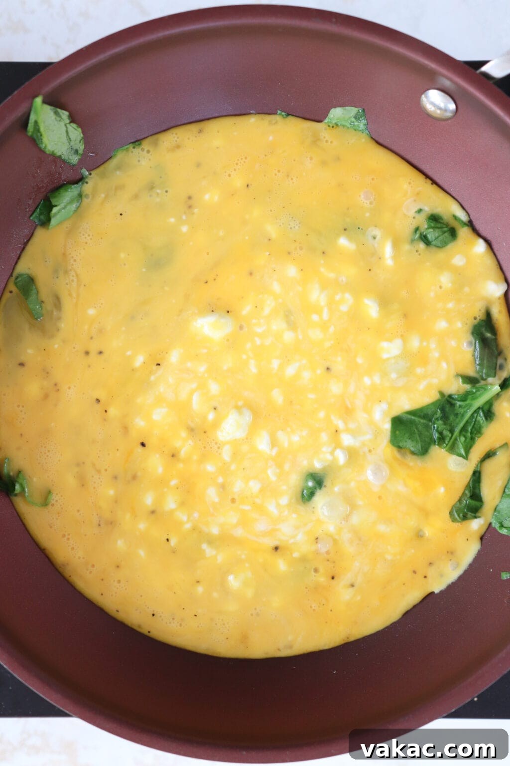 Dreamy 10-Minute Cottage Cheese Scramble 6 The whisked egg and cottage cheese mixture being poured into a frying pan already containing wilted spinach, with the cooking process just beginning.