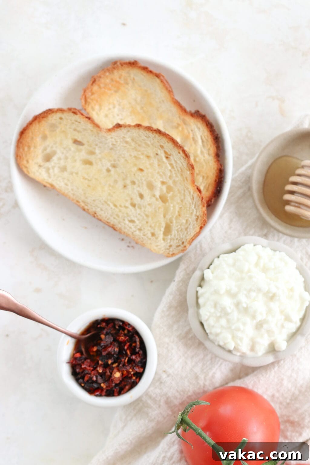 Two slices of toast surrounded by bowls containing honey, cottage cheese, and chili crisp oil.
