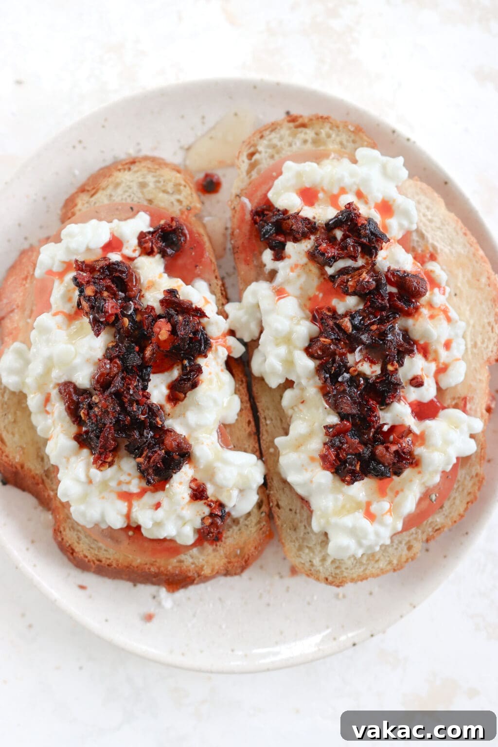Two pieces of toast topped with tomato, cottage cheese, chili crisp oil and honey on a plate