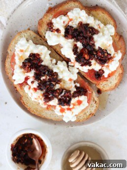 Two pieces of cottage cheese toast with heirloom tomato topped with chili crisp oil and honey on a plate.