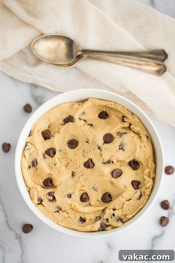 No-Bake Cookie Dough Delights 4 A white ceramic bowl filled with freshly made edible cookie dough, with two spoons resting beside it, inviting a taste.