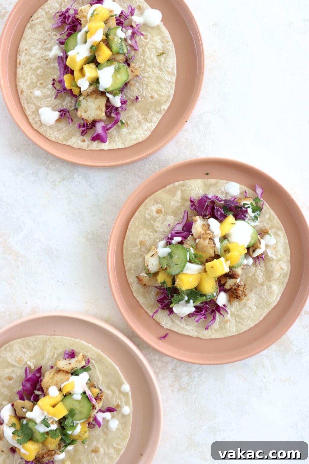 Easy 15-Minute Blackened Fish Tacos with Tangy Slaw 2 Three perfectly plated blackened fish tacos adorned with a fresh cabbage slaw, sweet mango, and crisp cucumber, served on stylish pink plates.