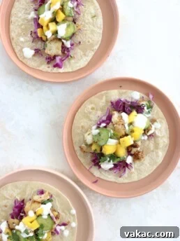 Three blackened fish tacos topped with cabbage slaw, mango and cucumber on pink plates.