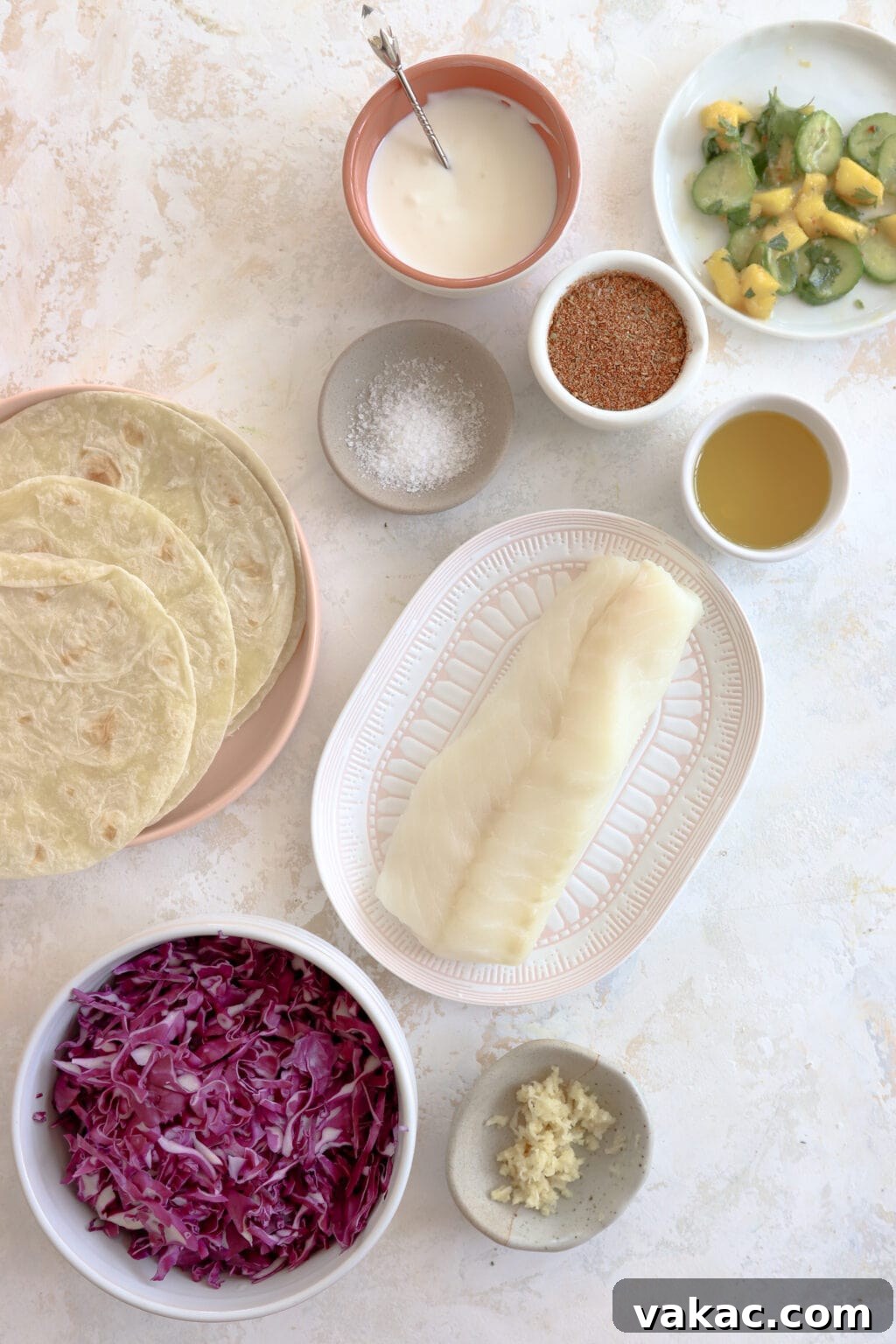 Easy 15-Minute Blackened Fish Tacos with Tangy Slaw 3 A vibrant display of ingredients for making delicious fish tacos, arranged in bowls and on plates. Featured items include a refreshing mango and cucumber salad, creamy lime crema, spicy Cajun seasoning, cooking oil, salt, soft tortillas, succulent white fish, crisp shredded cabbage, and aromatic garlic cloves.