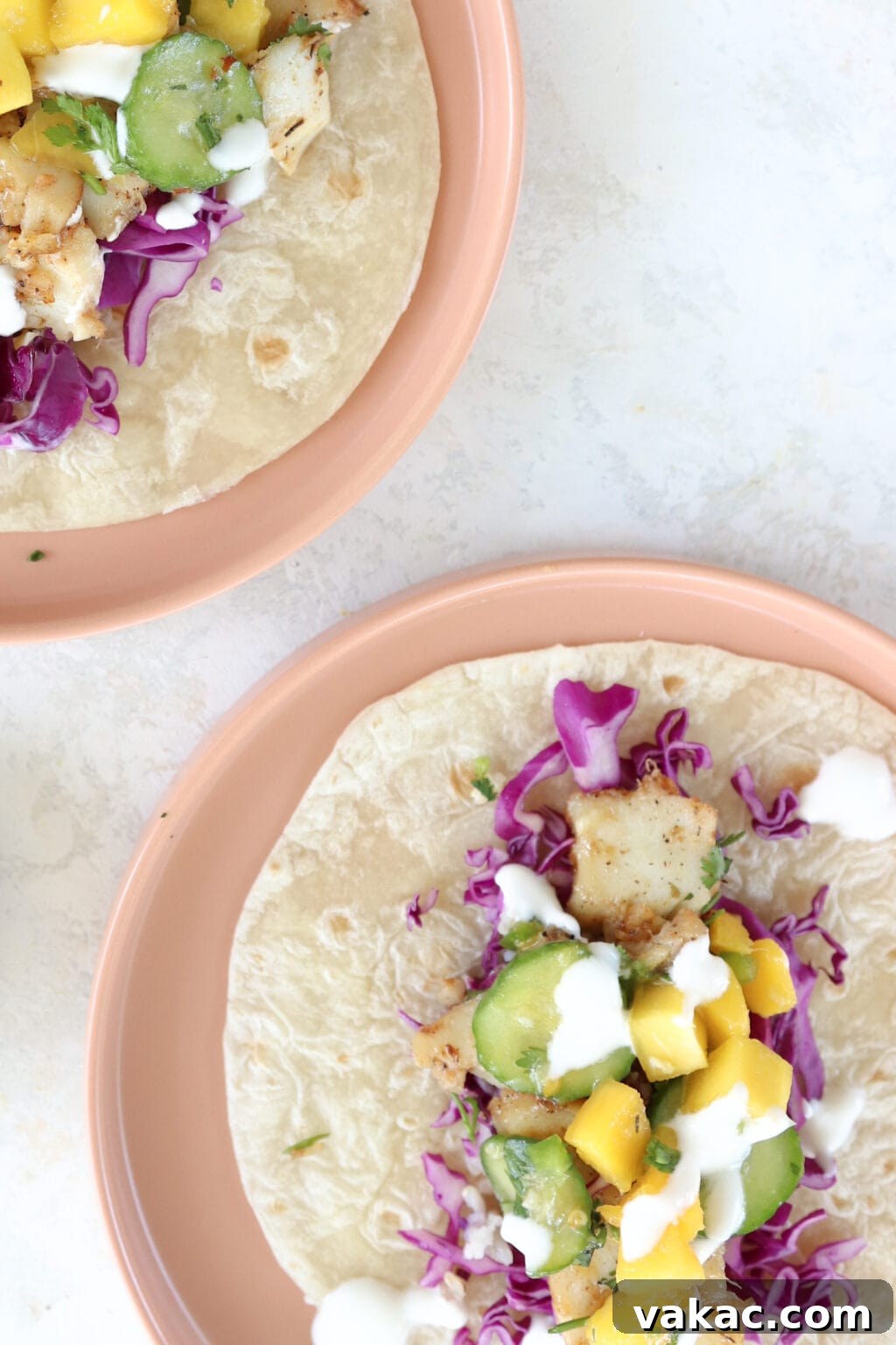 Easy 15-Minute Blackened Fish Tacos with Tangy Slaw 9 Two beautifully arranged fish tacos, showcasing a colorful filling of cabbage, mango, and cucumber, served on inviting pink plates.