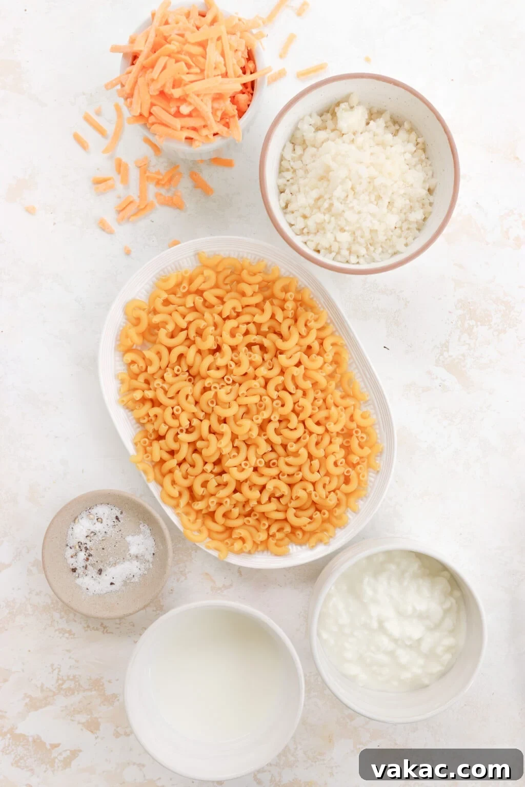 Secretly Creamy 5-Ingredient Cottage Cheese Mac 3 Ingredients for Creamy Cottage Cheese Mac and Cheese in white bowls, including elbow pasta, cottage cheese, milk, shredded cheddar cheese, garlic salt and cornstarch