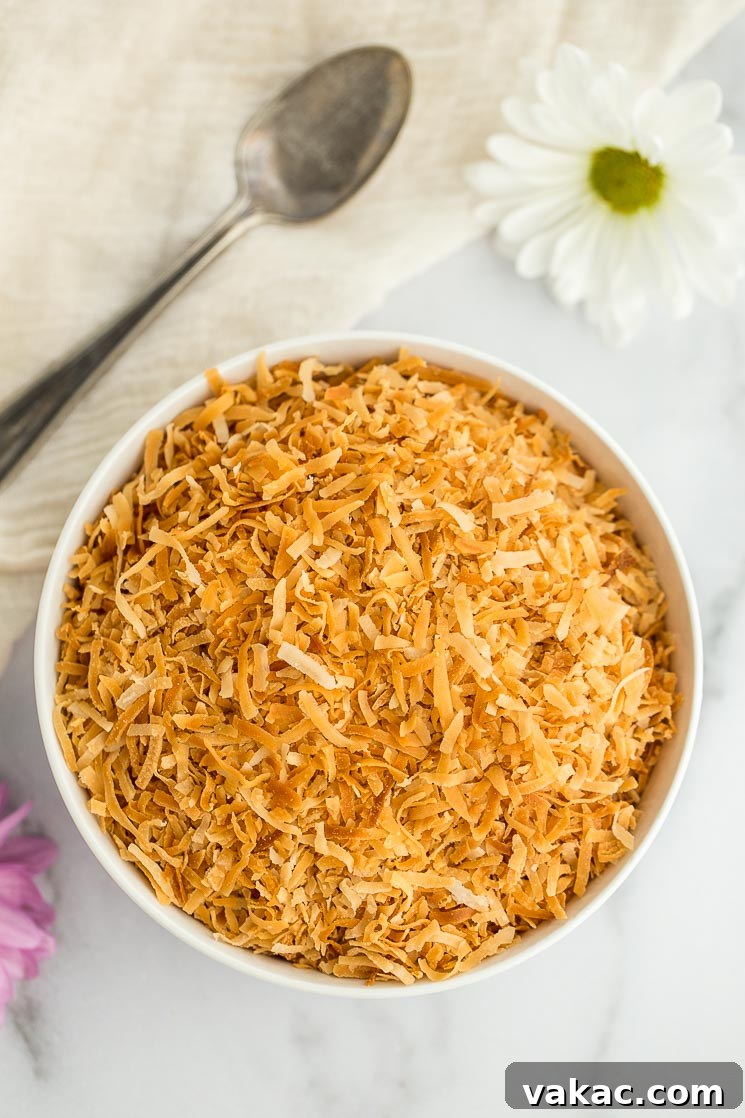 Secrets to Perfectly Toasted Coconut 2 A white bowl filled with toasted coconut with an antique spoon and flowers in the background.