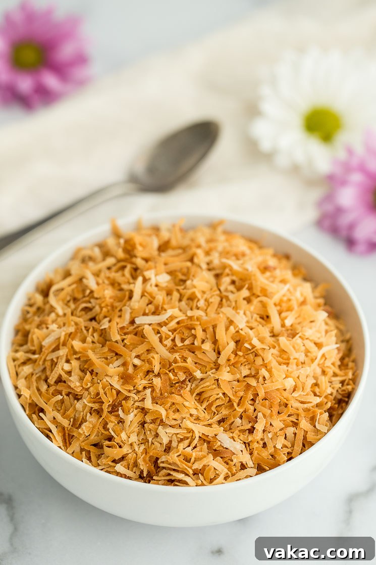 Secrets to Perfectly Toasted Coconut 6 A white bowl filled with toasted coconut with an antique spoon and flowers in the background.