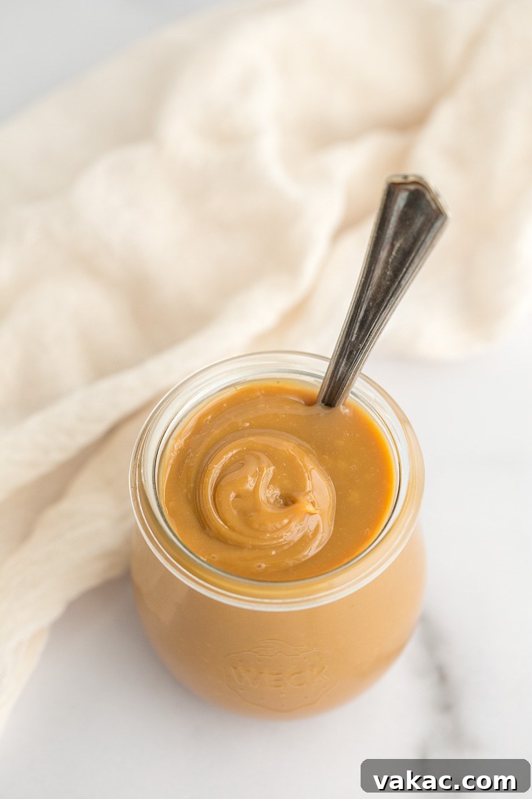 A glass jar filled with luscious homemade dulce de leche, ready to be enjoyed with an antique spoon.